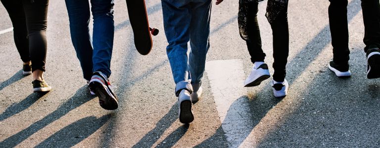 Zu sehen sind die Füße von ein paar Jugendlichen, die über die Straße laufen